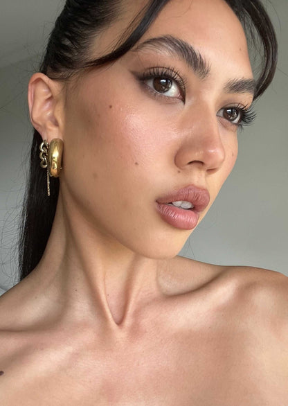 Close-up of a woman with bold eyeliner, gold hoop earrings, and smooth skin, showcasing a natural makeup look. Beauty and fashion portrait.