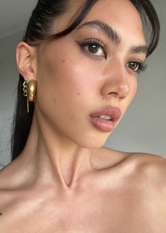 Close-up of a woman with bold eyeliner, gold hoop earrings, and smooth skin, showcasing a natural makeup look. Beauty and fashion portrait.