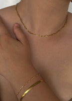 Gold chain necklace and bracelet on a woman's neck and wrist, minimalist jewelry, elegant fashion accessory, close-up, skin tone background.