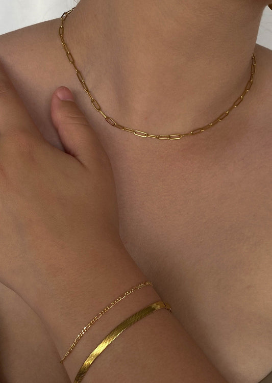 Gold chain necklace and bracelet on a woman's neck and wrist, minimalist jewelry, elegant fashion accessory, close-up, skin tone background.