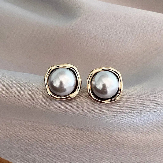 Elegant pearl stud earrings with gold-tone settings on a soft satin background, showcasing luxury jewelry fashion and timeless style.
