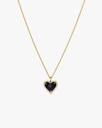 Gold chain necklace with a heart-shaped black gemstone pendant, surrounded by small clear crystals, on a white background. Elegant jewelry accessory.