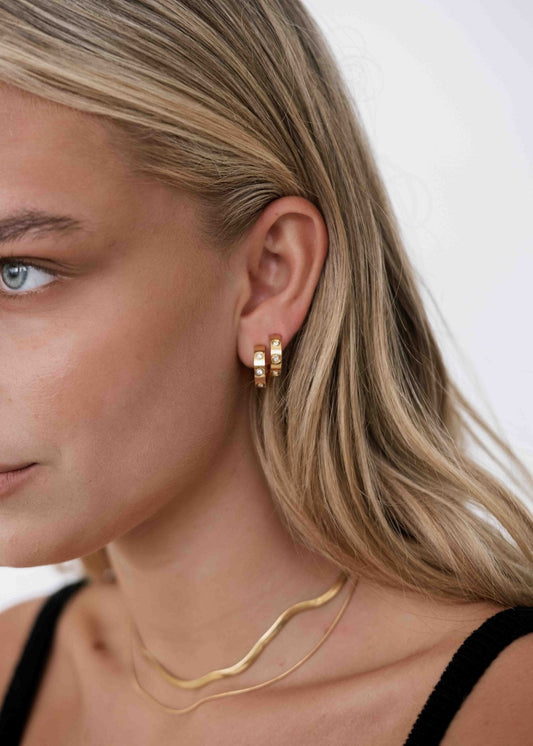 Close-up of a woman wearing gold hoop earrings and a gold necklace, showcasing elegant jewelry fashion. Blonde hair, minimalistic style.