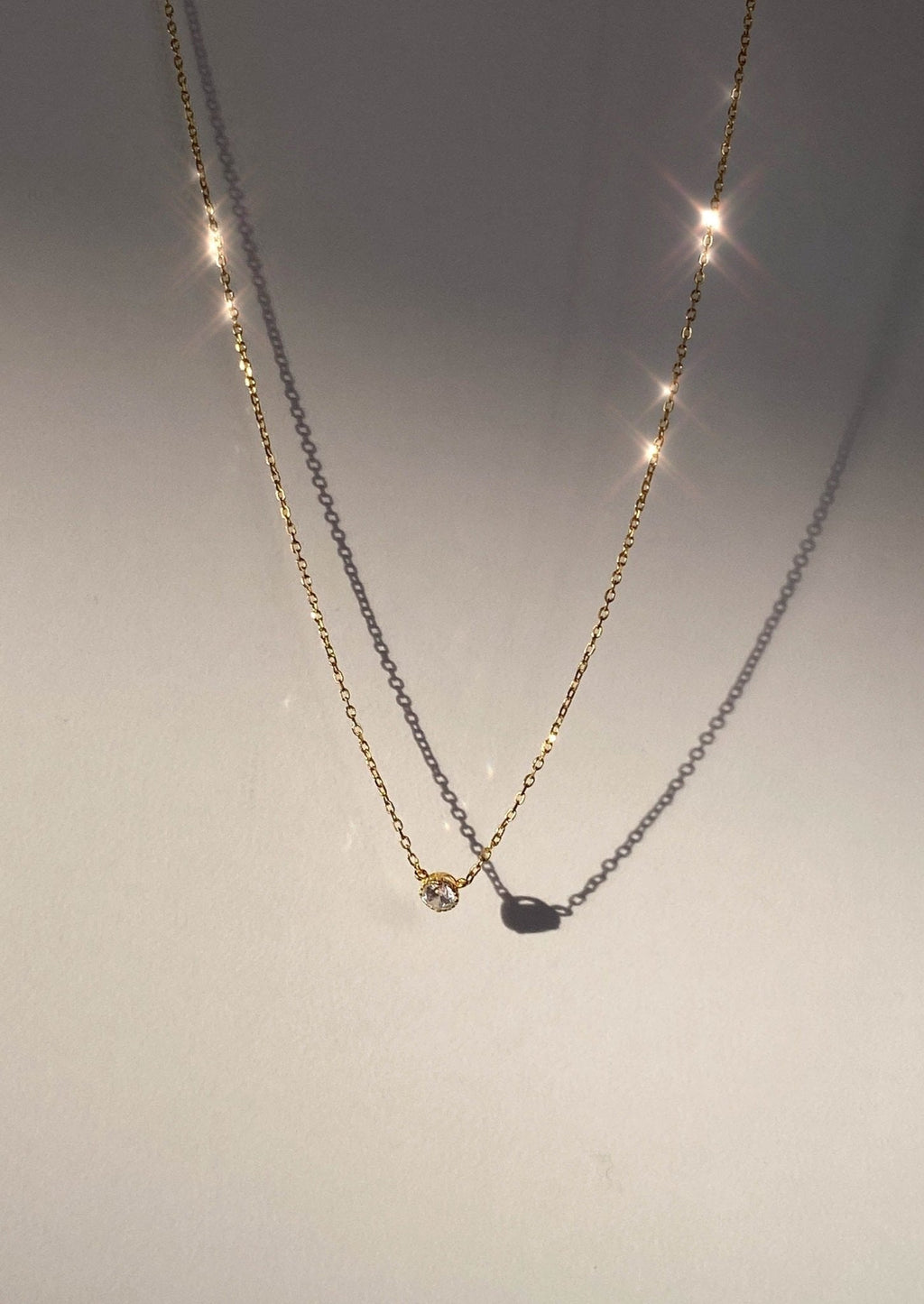 Gold necklace with a single sparkling diamond pendant casting a shadow, illuminated by soft light. Elegant jewelry, minimalist design, luxury accessory.