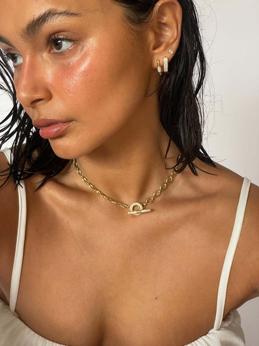 Woman wearing gold chain necklace and hoop earrings, showcasing dewy skin and wet hair, dressed in a white top. Fashion jewelry and beauty portrait.