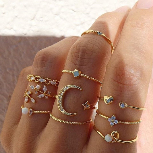 Close-up of a hand adorned with multiple gold rings featuring moon, star, heart, and floral designs, accented with gemstones and pearls.