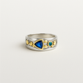 Silver ring with gold accents and blue and green gemstones on a light gray background