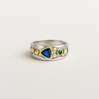 Silver ring with gold accents and blue and green gemstones on a light gray background
