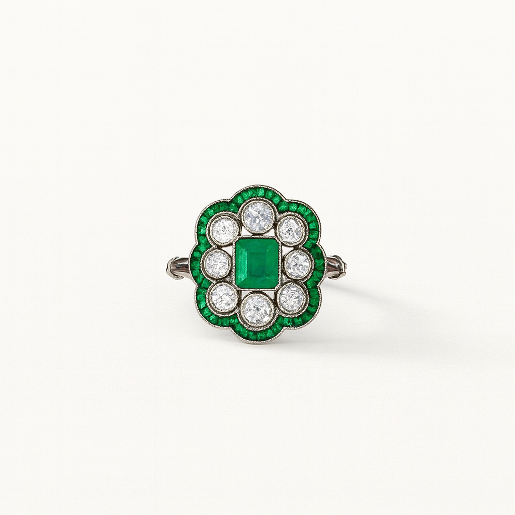 Vintage emerald and diamond ring with a central square-cut emerald, surrounded by round diamonds and emerald accents, set in a floral design.