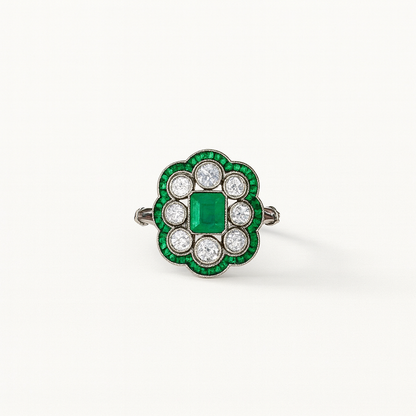 Vintage emerald and diamond ring with a central square-cut emerald, surrounded by round diamonds and emerald accents, set in a floral design.