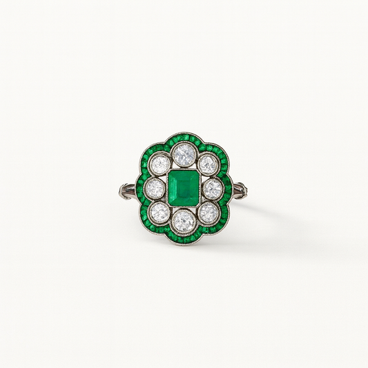 Vintage emerald and diamond ring with a central square-cut emerald, surrounded by round diamonds and emerald accents, set in a floral design.