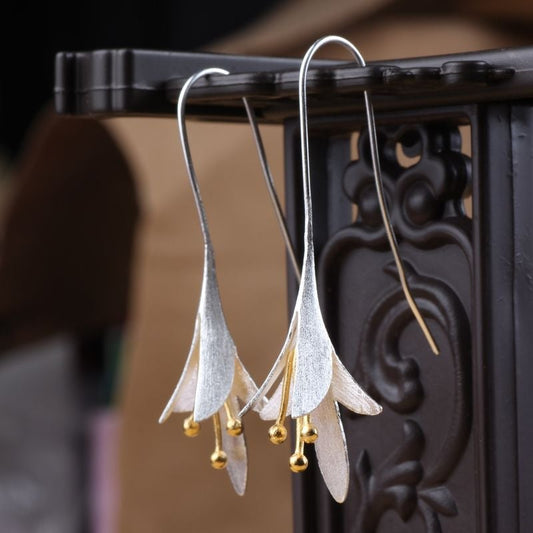 Elegant silver and gold flower drop earrings with delicate petal design, hanging on ornate metal stand. Perfect for fashion and jewelry enthusiasts.