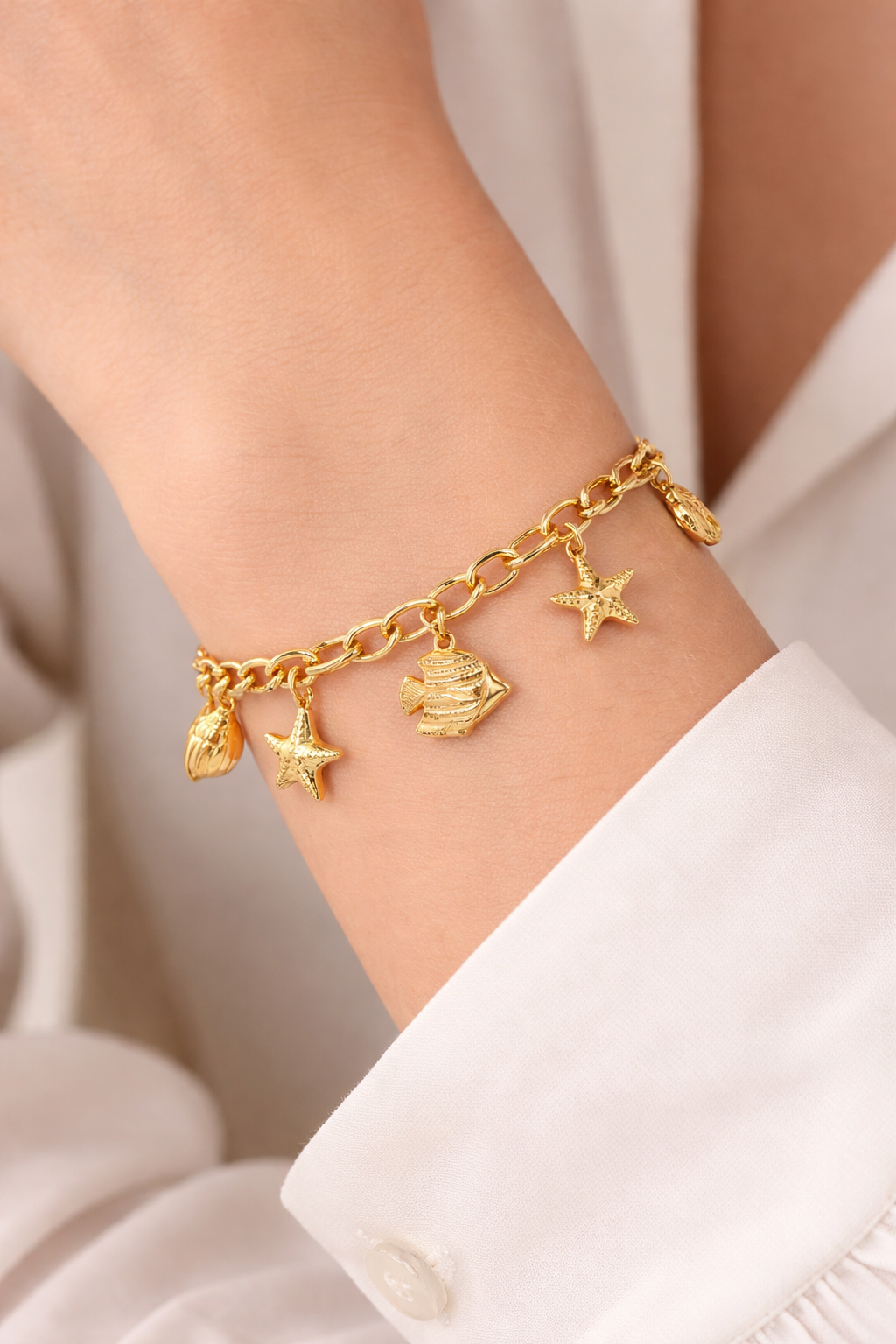 Gold charm bracelet on a wrist with a neutral background