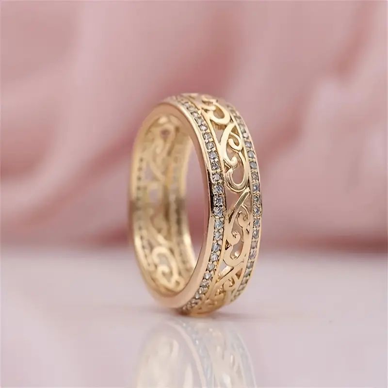 Elegant gold ring with intricate filigree design and diamond accents, set against a soft pink background. Luxurious jewelry, perfect for weddings.