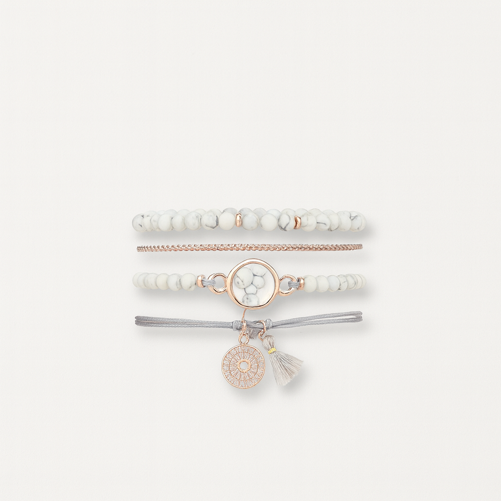 Stacked white and gold beaded bracelets with a central marble charm and tassel, featuring a bohemian style on a neutral background.