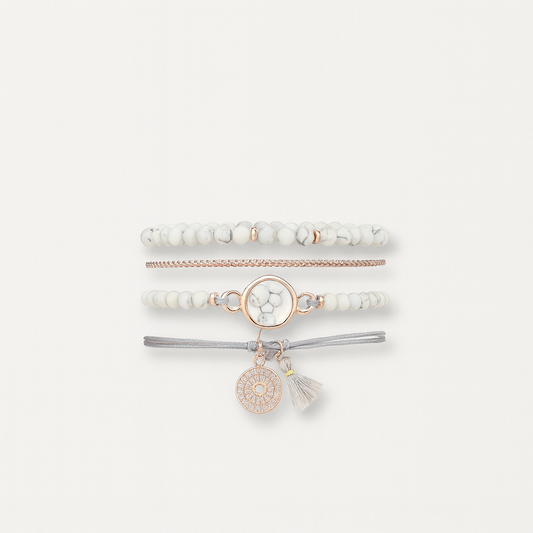 Stacked white and gold beaded bracelets with a central marble charm and tassel, featuring a bohemian style on a neutral background.