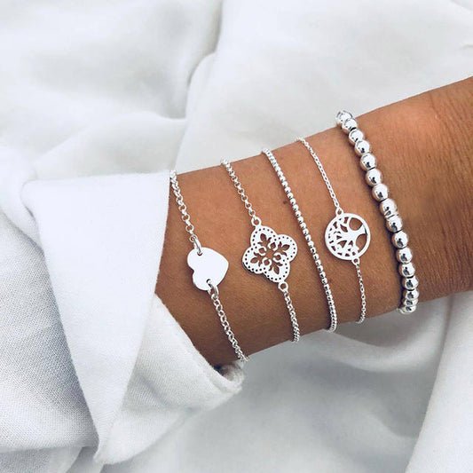 Silver charm bracelets on wrist, featuring heart, floral, and geometric designs, paired with a beaded bracelet. Elegant jewelry fashion accessory.