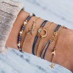 A wrist adorned with layered gold and blue bracelets featuring star, moon, and bead designs on a cozy sweater background. Fashionable jewelry accessories.
