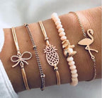 Four stylish gold and pink bracelets on wrist, featuring bow, pineapple, elephant, and flamingo charms, with beads and chain details. Fashion accessories.