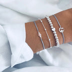 Four elegant silver bracelets on a wrist, featuring beads, heart charm, and minimalist designs, perfect for fashion and jewelry enthusiasts.