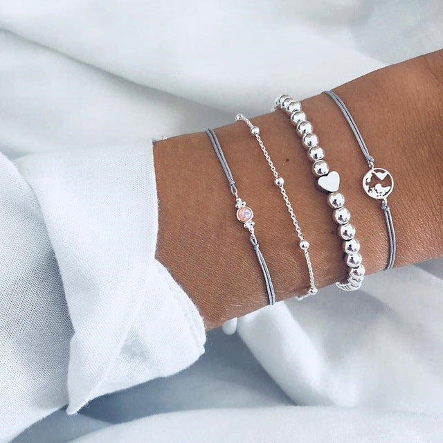Four elegant silver bracelets on a wrist, featuring beads, heart charm, and minimalist designs, perfect for fashion and jewelry enthusiasts.