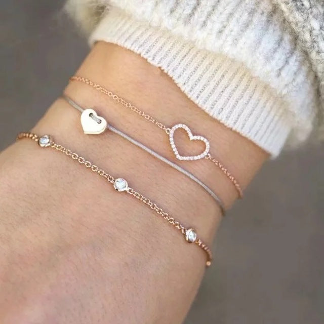 Delicate layered bracelets on wrist, featuring heart charms and sparkling stones. Elegant jewelry, rose gold and silver tones, fashion accessory.