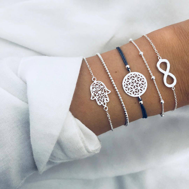 Silver and blue charm bracelets on wrist, featuring Hamsa, flower of life, infinity symbols. Stylish jewelry, fashion accessories, elegant design.