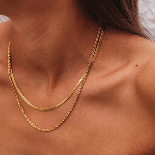 Gold layered necklaces on woman's neck, featuring a sleek herringbone chain and a twisted rope chain. Fashion jewelry, elegant accessory.