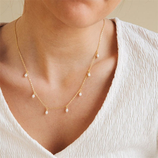 Gold necklace with small pearl pendants on a woman's neck, wearing a textured white top. Elegant jewelry, minimalist fashion accessory.