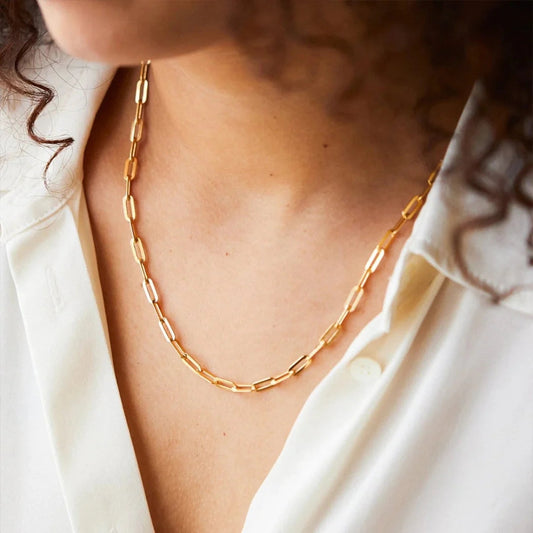 Gold chain necklace on woman wearing white shirt, close-up. Elegant jewelry, fashion accessory, minimalist style, perfect for everyday wear.