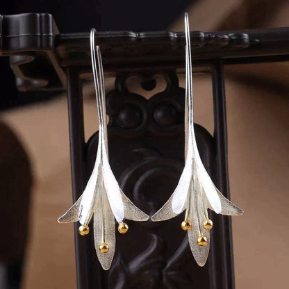 Elegant silver drop earrings with floral design and gold bead accents, hanging on a decorative stand. Perfect for fashion and jewelry enthusiasts.