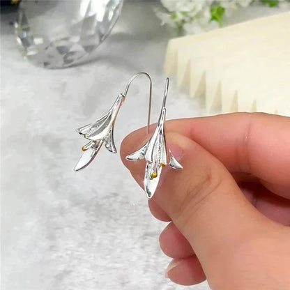 Silver lily flower earrings with hook design, held in hand. Elegant jewelry, floral motif, perfect for fashion accessories and gift ideas.