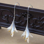 Elegant silver drop earrings with floral design and gold bead accents, displayed on ornate dark wood background. Fashion jewelry accessory.