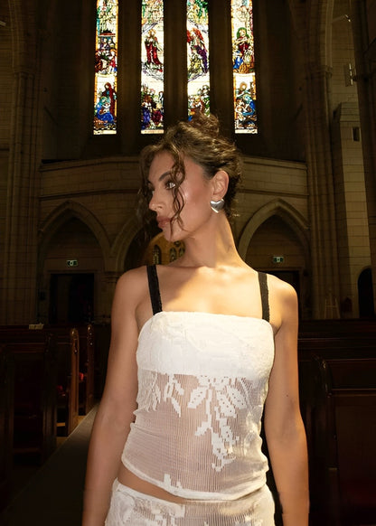 Woman in a white lace dress standing in a church with stained glass windows.