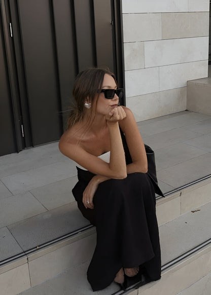 Woman in a black dress sitting on steps with a neutral wall background