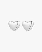 Silver heart-shaped stud earrings on a white background, minimalist jewelry design, perfect for everyday wear, elegant and timeless accessory.