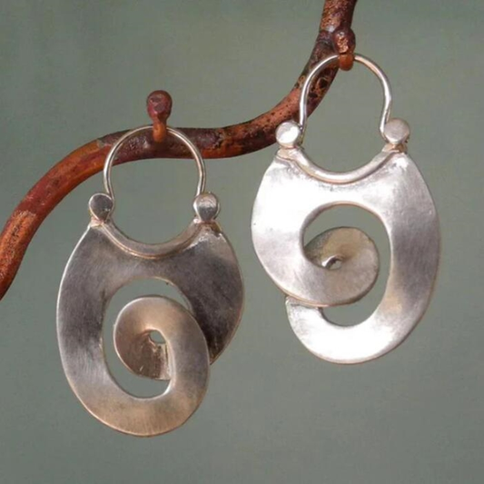 Silver spiral earrings hanging on a branch with a green background