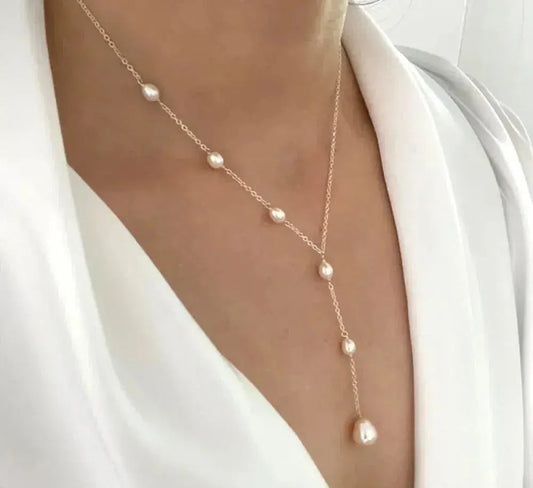 Elegant pearl drop necklace on woman wearing white blouse; delicate gold chain with evenly spaced pearls, perfect for fashion and jewelry enthusiasts.