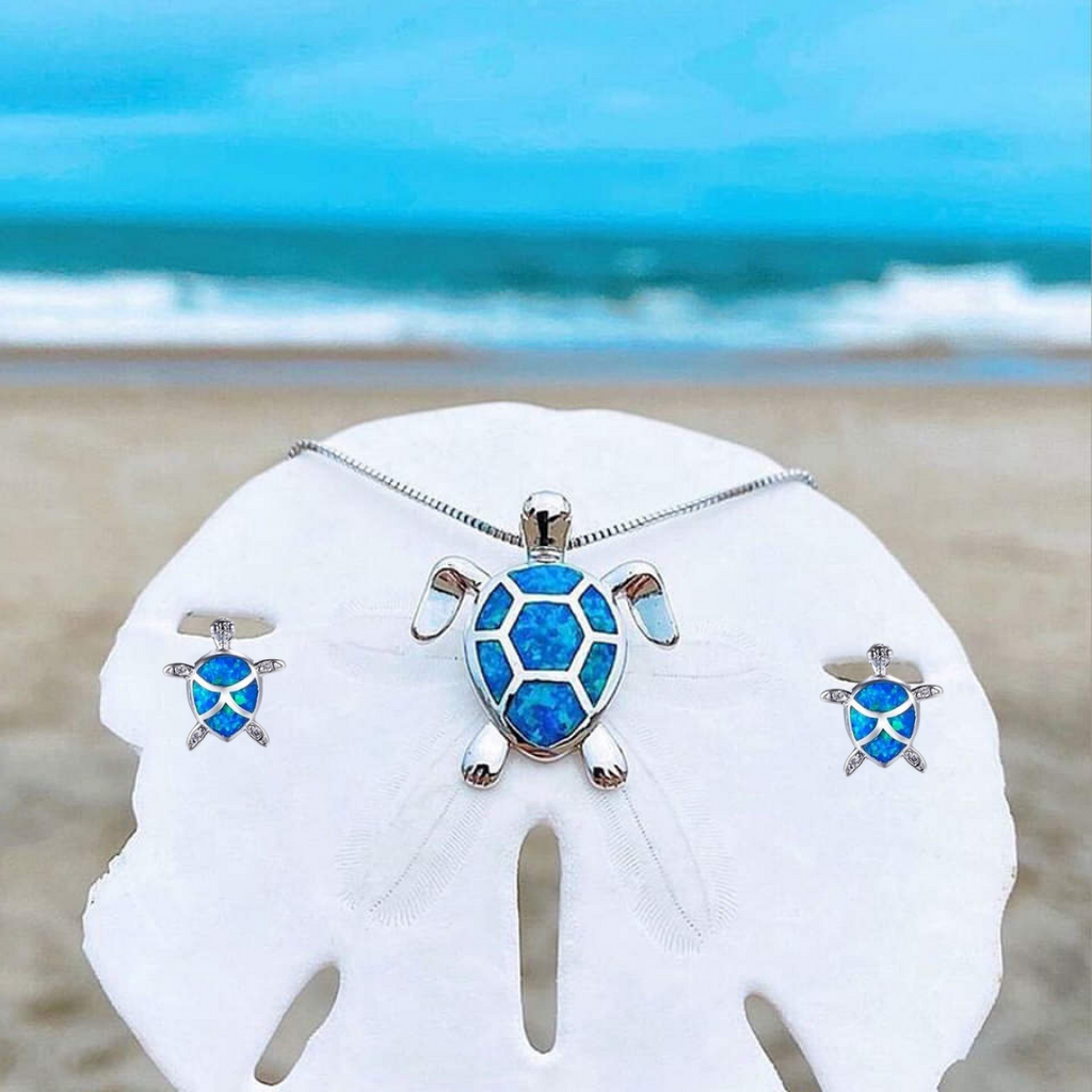 Turtle jewelry set with blue opal inlay on a sand dollar at the beach, featuring a necklace and earrings, ocean background, beach fashion accessory.