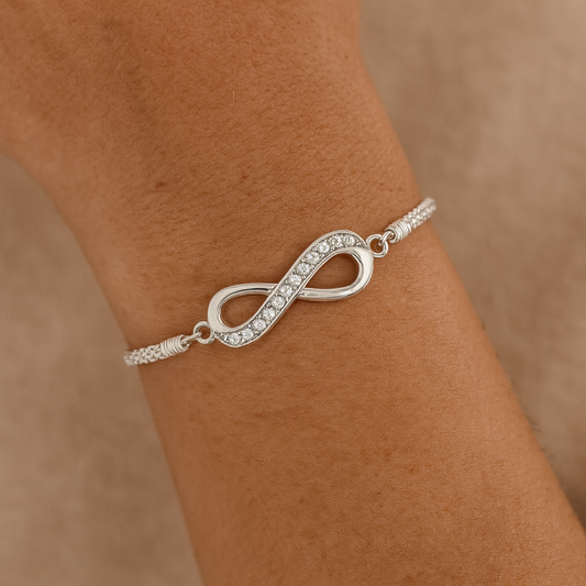Silver infinity bracelet with clear stones on a wrist against a beige background