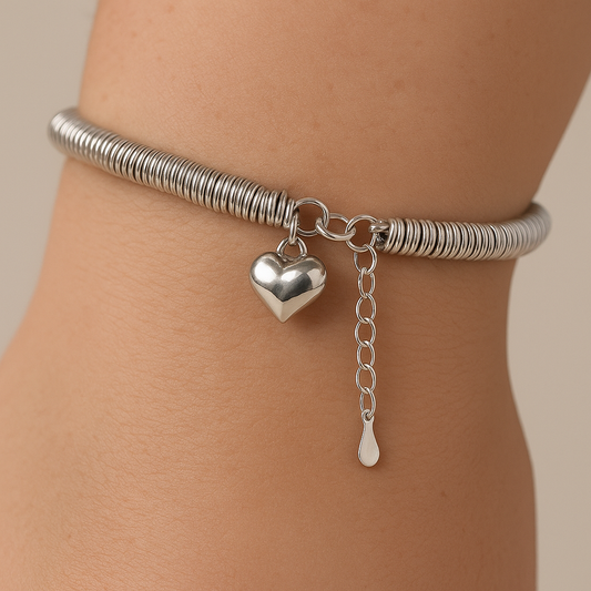 Silver anklet with heart and drop charm on a person's ankle against a neutral background