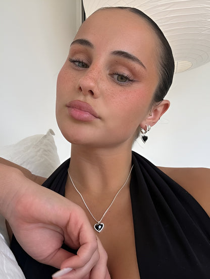 Woman wearing a black top with a heart-shaped pendant necklace and earrings.