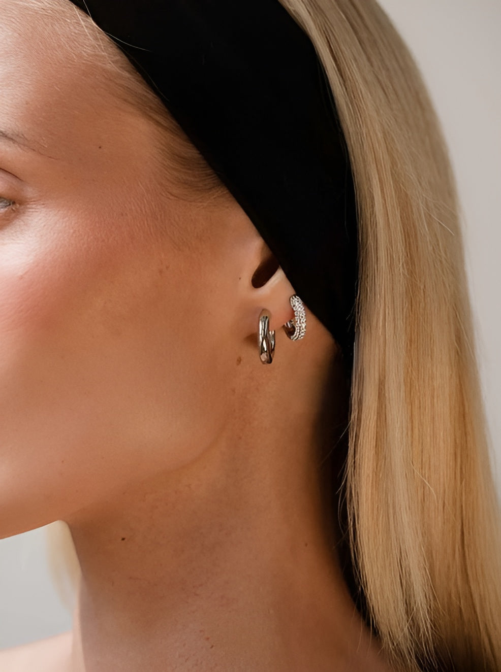 Close-up of a person wearing gold hoop earrings with a neutral background