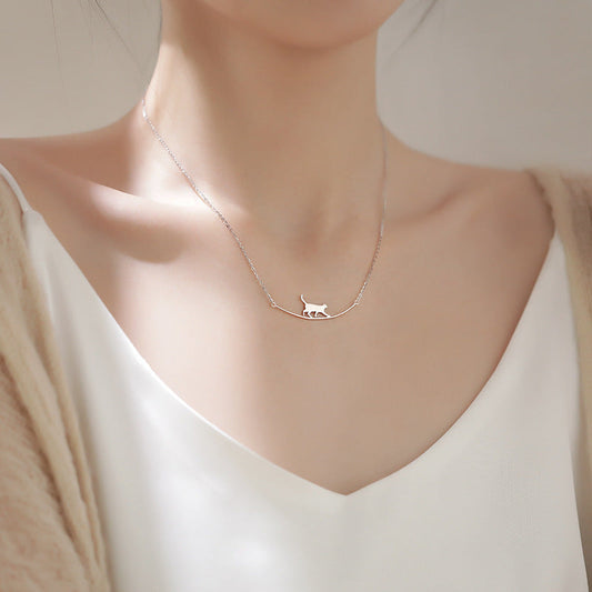 Elegant silver cat necklace on woman's neck, minimalist jewelry design, perfect for cat lovers, fashion accessory, delicate chain, white top.