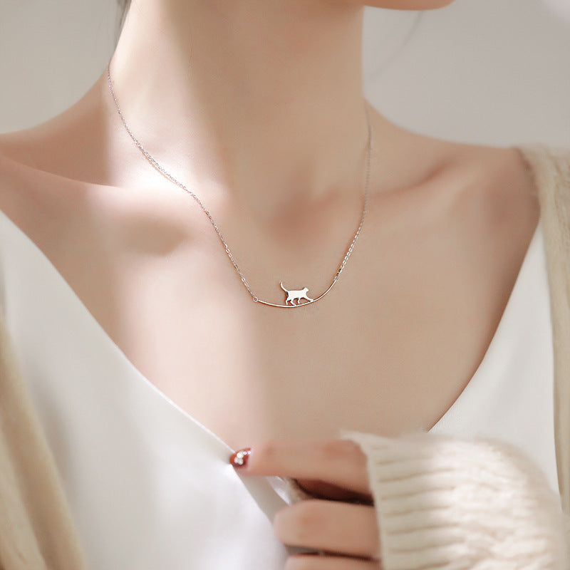 Delicate silver necklace with a minimalist cat pendant on a woman's neck, wearing a white top and beige cardigan. Elegant jewelry fashion accessory.