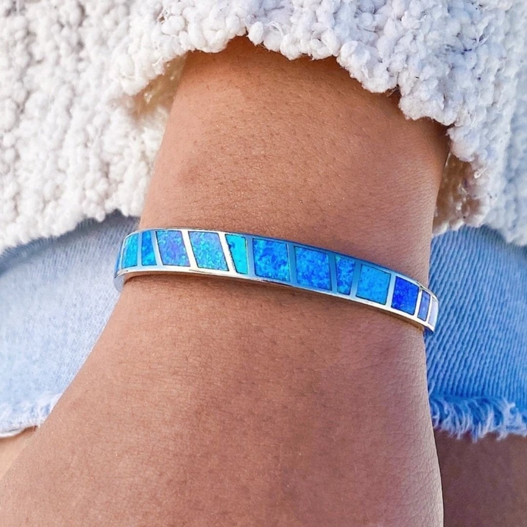 Close-up of a wrist wearing a blue opal inlay bracelet with silver accents, paired with a textured white sweater and light denim, showcasing elegant jewelry fashion.