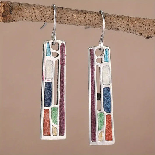 Colorful geometric mosaic earrings with silver hooks, featuring rectangular shapes and vibrant inlays, hanging from a branch.