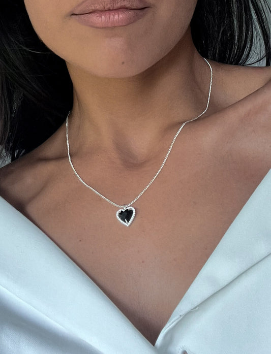 Woman wearing a silver heart-shaped black gemstone necklace on a white blouse, showcasing elegant jewelry fashion.