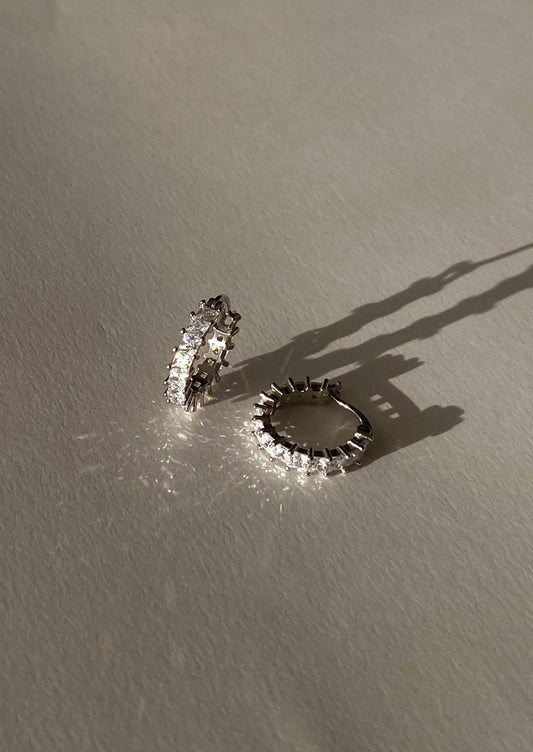 Elegant diamond hoop earrings casting shadows on a neutral surface, showcasing luxury jewelry design and sparkling gemstones in natural light.