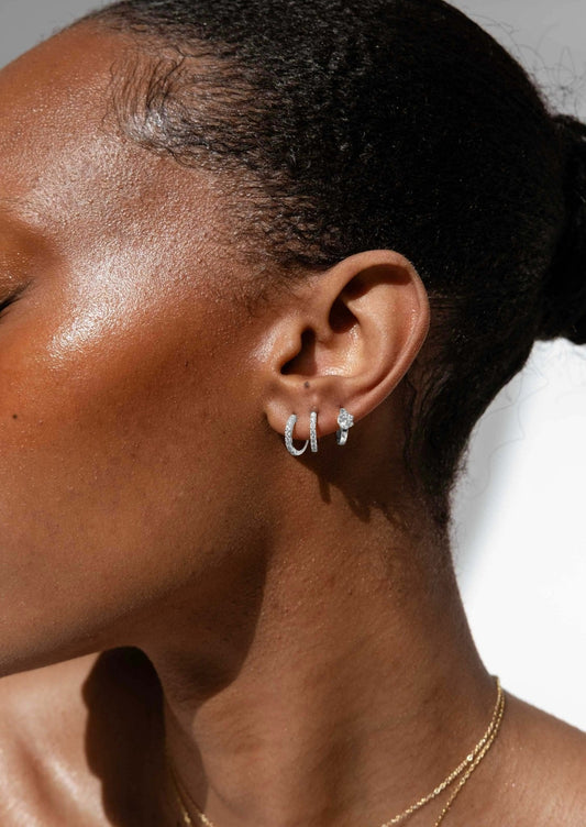 Close-up of a woman's ear adorned with silver hoop earrings and a diamond stud, showcasing elegant jewelry against smooth, glowing skin.